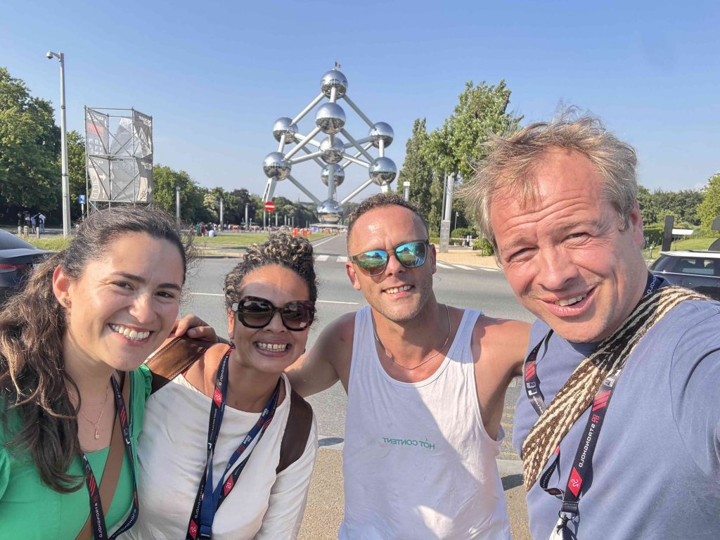 Cuatro profesionales del café sonríen en un selfie frente al Atomium de Bruselas, con acreditaciones de World of Coffee, en un día soleado